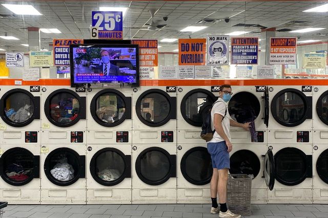 Inside a laundromat, a man in a mask and the news on the tv set